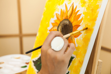 Artist's hand with brush and palette painting a picture Sunflowerの写真素材