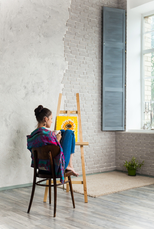 The young beautiful girl painter with a cup of coffee sit on table in the workshop.の写真素材