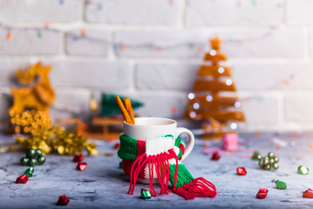 Mug Of Hot Coffee Or Tea with mini marshmallows and cinnamon with green red white scarf against a rustic background with beautiful Christmas lights of bokeh with toysの写真素材