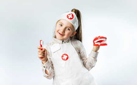Little cool doctor dentist girl in a medical suit with a toy jaw and Toothbrushの写真素材