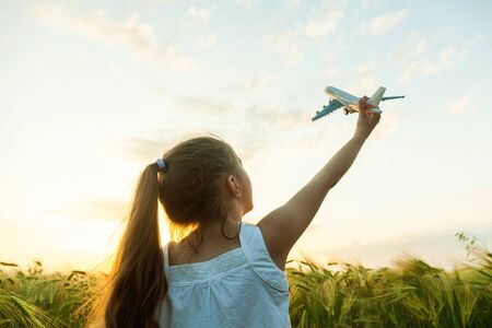 Little girl holding airplane toy during running in the green wheat field during summer dayの写真素材