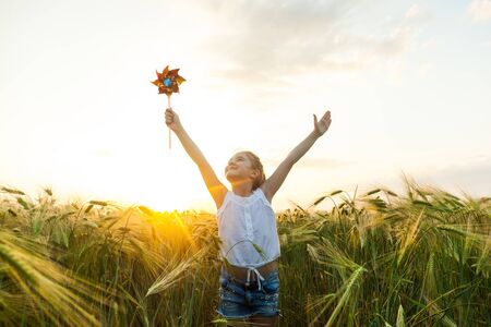 Little girl playing on the meadow on sun with windmill in her hands. Child holding wind toy on wheat field.の写真素材