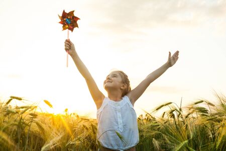 Little girl playing on the meadow on sun with windmill in her hands. Child holding wind toy on wheat field.の写真素材