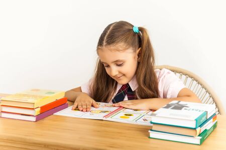 Six years old child reading a book at home, reflects on lessons. Girl studing at table on white backgroundの写真素材