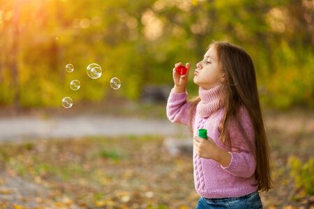 Caucasian child girl blowing soap bubbles outdoor at sunset - happy carefree childhoodの写真素材