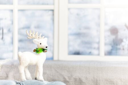 A snow-white toy deer stands on a windowsill. The window is snowyの写真素材