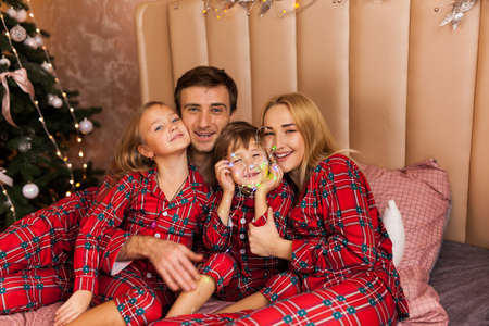 Family in pajamas lying on bed. Mother, father and two children having fun in bedroom. Xmas and New Year conceptの写真素材