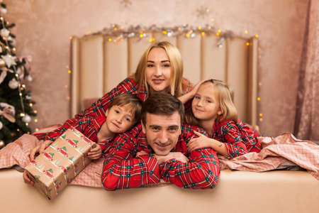 Family portrait in pajamas lying on bed. Mother, father and two children having fun in bedroom. Xmas and New Year conceptの写真素材