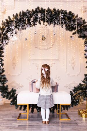 Portrait of a beautiful little girl with a bow on her hair in the interior with Christmas decorations and gift boxes.の写真素材