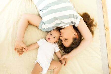 Top view of a happy mother kissing a baby lying on a bed.
