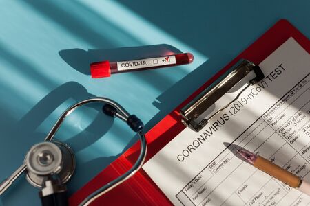 Coronavirus blood test concept in clinic, test tube with coronavirus on the doctor table with medical card and stethoscope.の写真素材