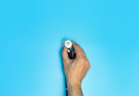 Doctors Hand Holding up a Stethoscope over blue backgroundの写真素材