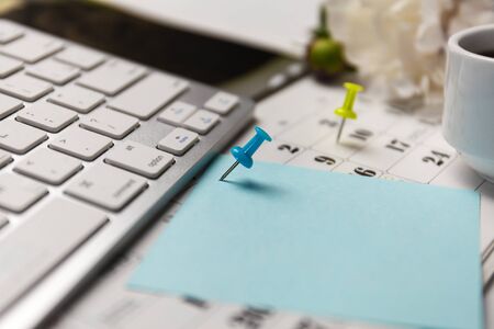 A blue color pin on calendar, keyboard, blank blue paper and pencil. Concept for events planner is...