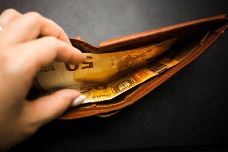 Woman's hand hand takes out banknotes from a brown wallet with euro money. Soft focusの写真素材