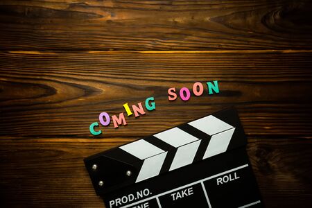 Coming soon Word made from multi-colored wooden letters on a brown wooden background and movie clapperboard. Filmmaking conceptの写真素材