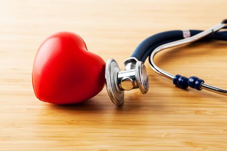 Listen to the heart. Stethoscope and red heart on wooden table. Cardiology concept