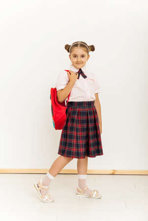 Full length portrait of a schoolgirl in uniform with backpack standing on white backgroundの写真素材