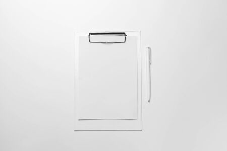 White clipboard with blank sheet of paper and pen on white table. Top view office accessories...