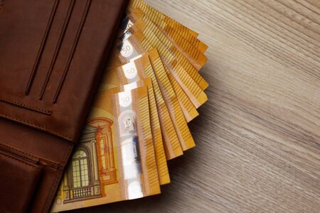 Wallet stuffed with Euro banknotes on the wooden table. Stuffed Leather Wallet. Euro Bills in...