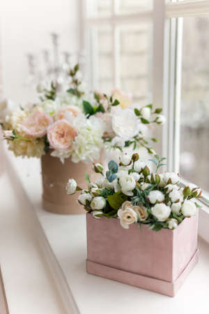 Beautiful delicate pink and white flowers in hat gift boxes stand on the sunny windowsill of the bedroom.の写真素材