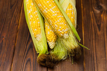 Fresh sweet corn on cobs with leaves on wooden table, closeup, top view. Fresh yellow corns ears...