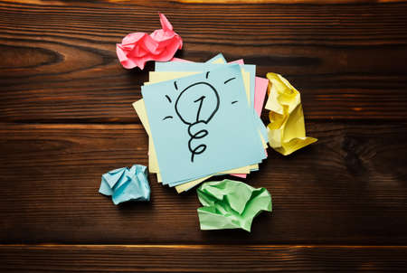 Drawn light bulb sticky note surrounded by crumpled paper on wooden table