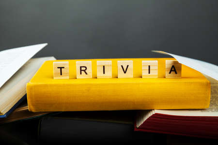 The concept of trivia knowledge. Trivia word from wooden blocks with letters on old and new books are piled up in a careless pile for uselessness, Much knowledgeの写真素材