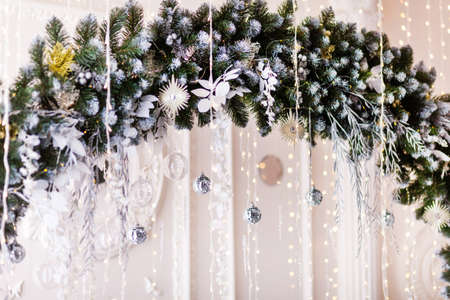 Decorative arch made of spruce branches, decorated with stylish baubles and balls, against the background of a white wall, in the interiorの写真素材