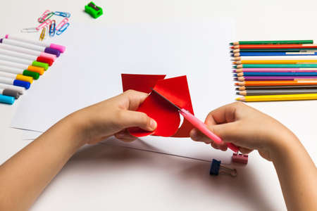 Child hands cutting a red heart out of paper with scissors at the table.の写真素材