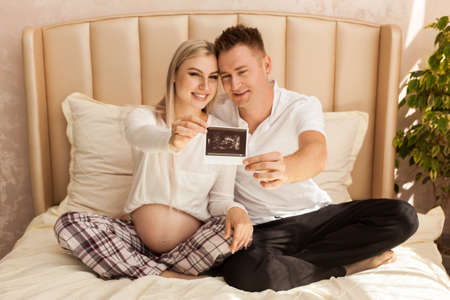 Happy parents holding babys ultrasound photo smiling at home. Focus on ultrasound image