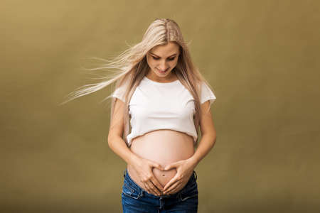 Pregnant happy Woman touching her belly. Pregnant mother portrait, caressing her belly and smiling. Healthy Pregnancy concept, blond expectant female on beige backgroundの写真素材