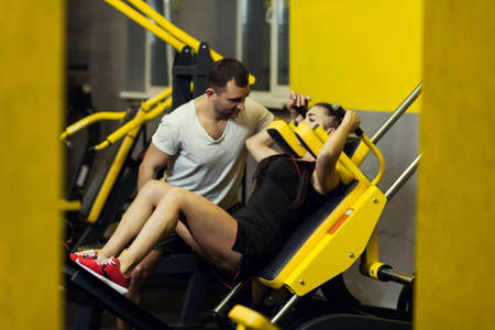 Sport, fitness, teamwork, weightlifting concept - young woman and personal trainer with flexing...