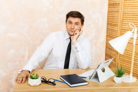 Luminous portrait of a middle age businessman in white shirt and tie. He is sitting at his desk,...