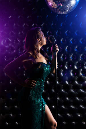 Young woman in beautiful dress with microphone and colorful lights on karaoke concert