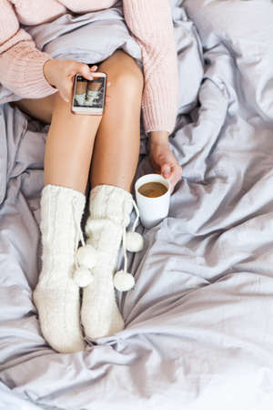 Woman resting keeping legs in warm socks on bed, takes a photo of breakfast for her profile on the social networkの写真素材
