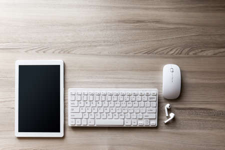 The office desk flat lay view with keyboard, mouse, tablet pc and wireless earphone on wood texture background.の写真素材