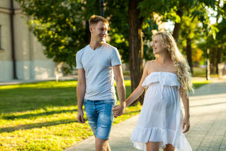 happy young pregnant woman with her husband walking in a city parkの写真素材
