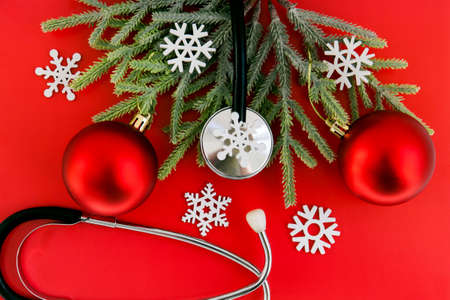 Medical Christmas and New Year. Stethoscope surrounded by red christmas tree balls and snowfalkes on red background. Concept for the New Year in medicineの写真素材
