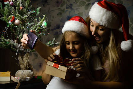 Child with Mother in Santa hats having a video call on christmas day, sitting on a couch in the living room with Christmas tree at homeの写真素材