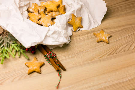 Christmas cookies in star shape in craft paper with pine branch and christmas decoration on the table in kitchenの写真素材