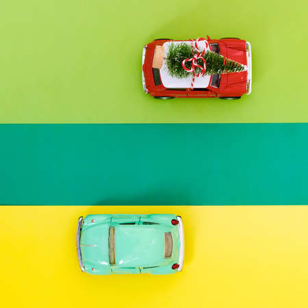 Minimal design for celebrating christmas or new year greeting card. Gift delivery concept. Little red and blue toy cars and Christmas tree on a green yellow backgroundの写真素材