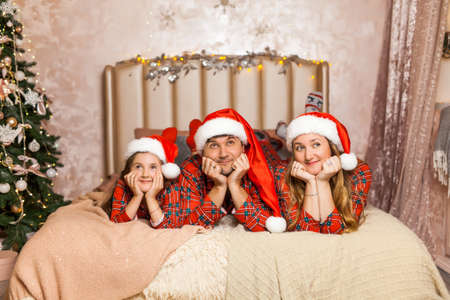 Family portrait in pajamas lying on bed. Mother, father little girl having fun in bedroom. Xmas and New Year conceptの写真素材