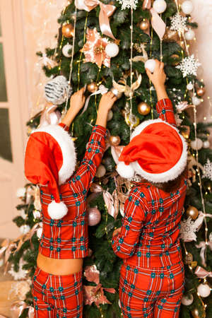 Happy little Two kids in red plaid pajamas and hats decorate the Christmas tree in beautiful living room.の写真素材