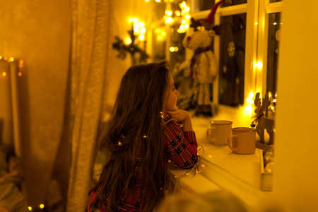magical mysterious girl child with a can with a luminous garland, classic dark background and warm light. concept of expectation of christmas, cozy warm styleの写真素材