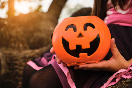 girl holding Halloween pumpkin jack o'lantern with sweet candy in hands. Halloween celebration conceptの写真素材