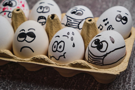Easter holiday eggs in masks. Tray of white eggs with drawn funny faces wearing medical masks at Easter holiday during virus epidemy close upの写真素材
