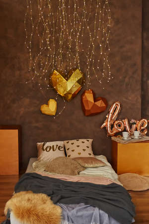 Romantic interior in brown colors with bed, pillows, blankets and Garland. Wooden tray with cups. 3d hearts on the wall. Selective focusの写真素材