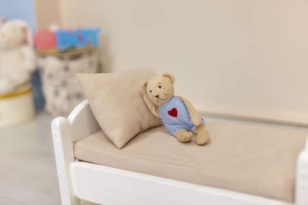 Little teddy bear on White wooden dooll's toy bed With pillow in kid's roomの写真素材