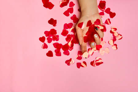 Romantic manicure and petals hearts, beautiful hands with creative manicure nails, white gel polish, lips and XO design, on pink background, place for textの写真素材