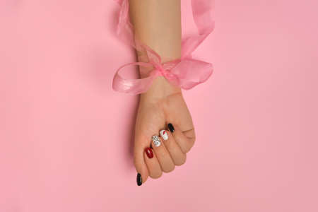 Close up view of beautiful female hand tied with a bow. creative manicure nails, white gel polish, lips and XO design, on pink background, place for textの写真素材